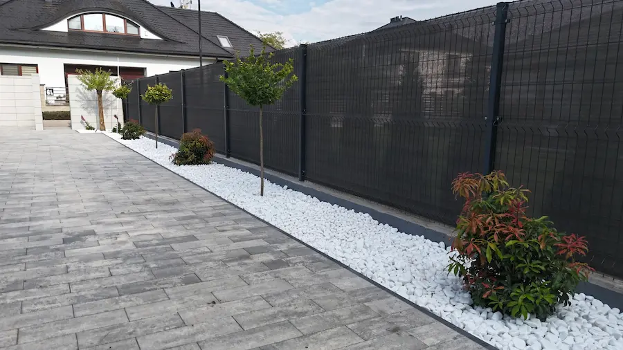 Gotowa rabata przy ogrodzeniu w Siedlcach — szara kostka brukowa, pas białego kamienia, drzewka i krzewy ozdobne po nasadzeniach i wykończeniu ogrodu przez Ziemne.net.